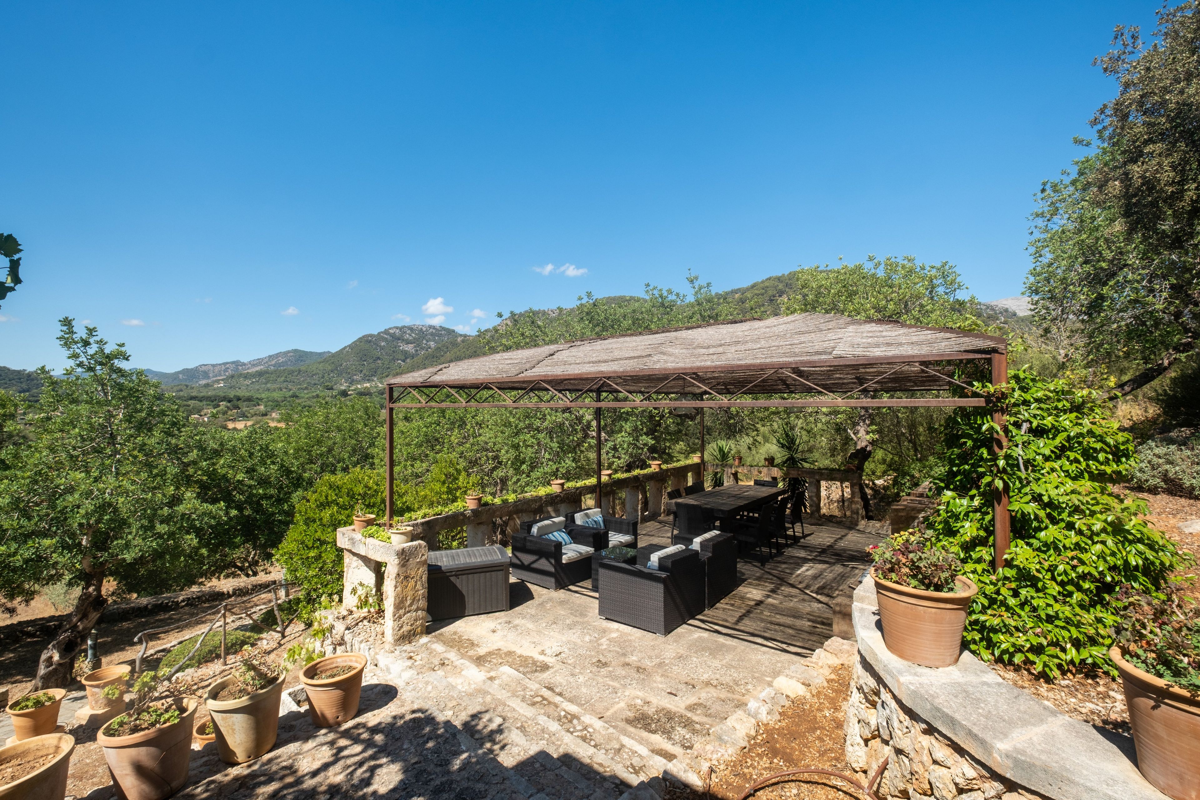 Un patio exterior con una pérgola, asientos y plantas en macetas.
