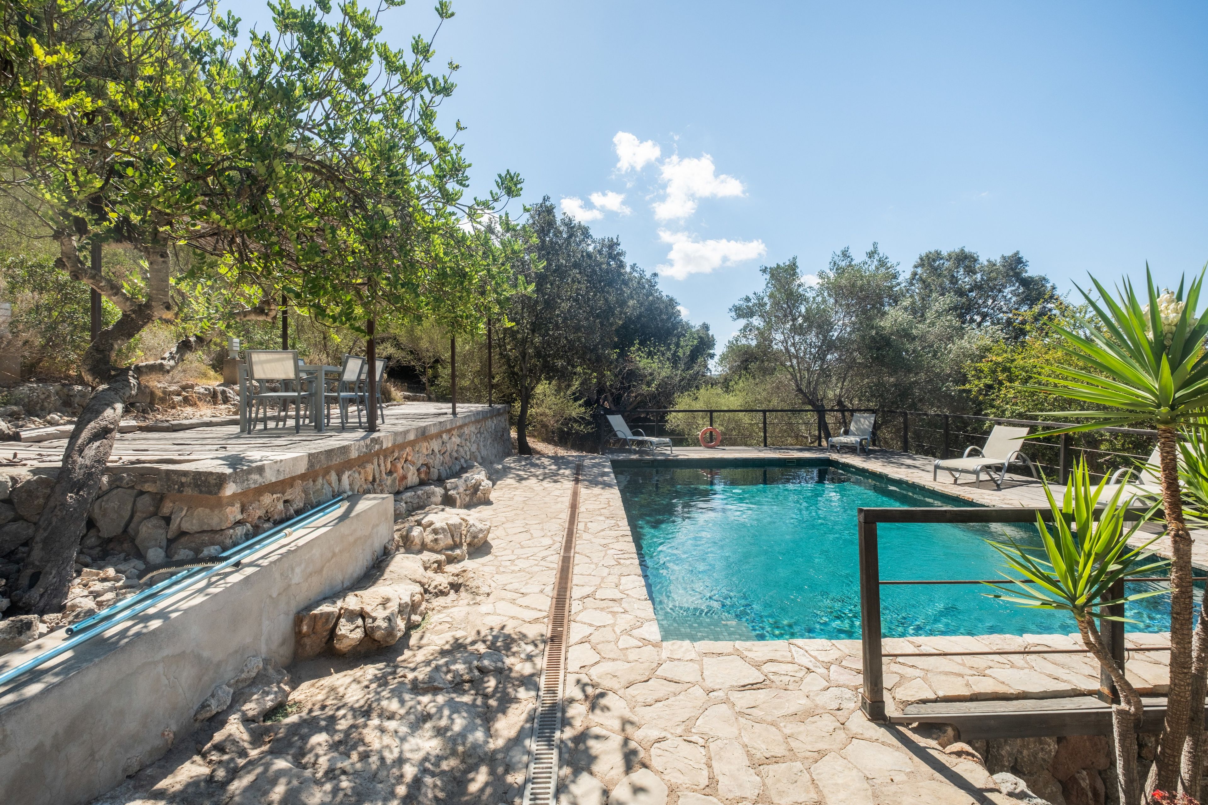 A swimming pool with stone tiles, surrounded by lounge chairs and a stone wall.