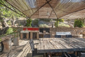 An outdoor patio with a stone wall, a grill, and a table with chairs.