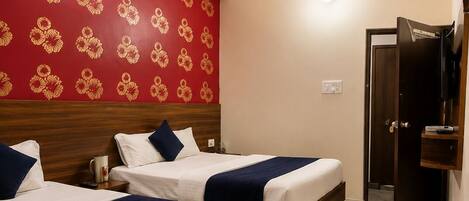 Une chambre d’hôtel avec deux lits, un ventilateur de plafond et un papier peint à motifs floraux rouges.
