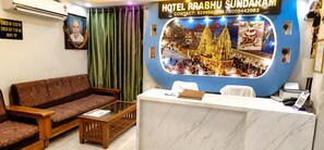 A hotel reception area with a check-in desk, a sofa, and a curtain. - Hotel Prabhu Sundaram Inn (Varanasi)