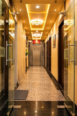 A hotel corridor with a marble floor, glass doors, and a reception desk. - Hotel Prabhu Sundaram Inn (Varanasi)