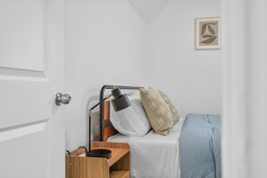 Ein Schlafzimmer mit einem Bett, einem Nachttisch, einer Lampe und einer Tür.