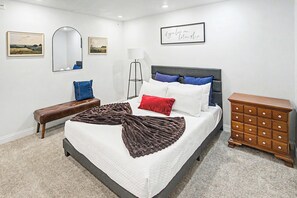 Un dormitorio con cama, un banco, cómoda, espejo y dos cuadros en la pared.