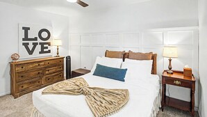 Ein ordentlich eingerichtetes Schlafzimmer mit Bett, Schminktisch, Nachttisch und einer Wand mit einem großen 'LOVE'-Schild.