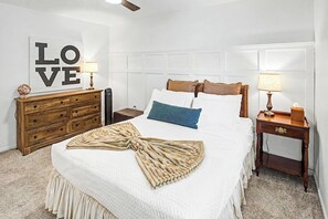 Ein ordentlich eingerichtetes Schlafzimmer mit Bett, Schminktisch, Nachttisch und einer Wand mit einem großen 'LOVE'-Schild.