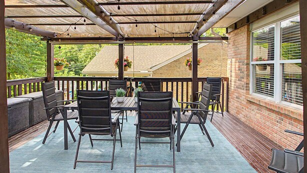 Eine überdachte Terrasse mit Tisch und Stühlen, einer Backsteinmauer und hängenden Blumenkörben.
