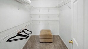 Ein begehbarer Kleiderschrank mit weißen Wänden, mehreren Regalen und einer Sitzbank.