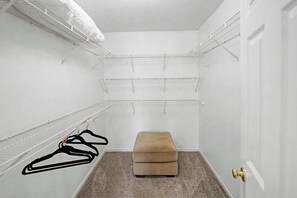 Ein begehbarer Kleiderschrank mit weißen Wänden, mehreren Regalen und einer Sitzbank.
