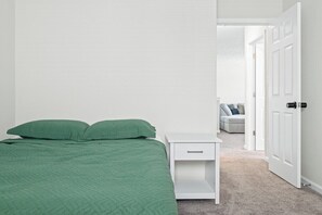A bedroom with a bed, a nightstand, and a door leading to another room. - Roadmap Lodging: 4BR on the Water, Patio & Grill (Columbus)