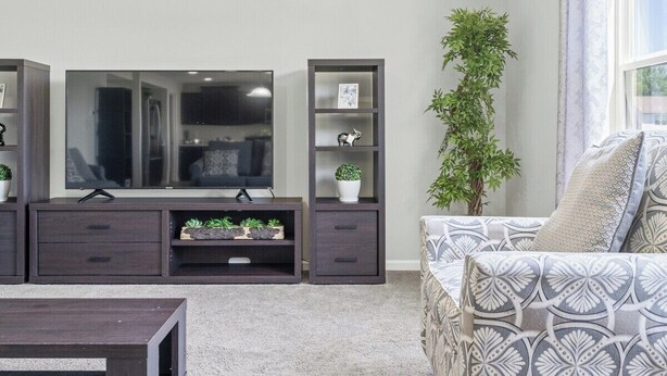 A living room with a flat-screen TV, dark wooden cabinets, a sofa, and a potted plant. - Roadmap Lodging: Modern Waterview, 4BR Lakefront Monthly, Pet OK (Columbus)