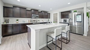 A modern kitchen with dark wood cabinets, stainless steel appliances, and a marble island with bar stools. - Roadmap Lodging: Modern Waterview, 4BR Lakefront Monthly, Pet OK (Columbus)