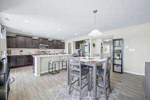 A modern kitchen with dark wood cabinets, a central island, and a dining area with a table and chairs. - Roadmap Lodging: 4BR on the Water, Patio & Grill (Columbus)