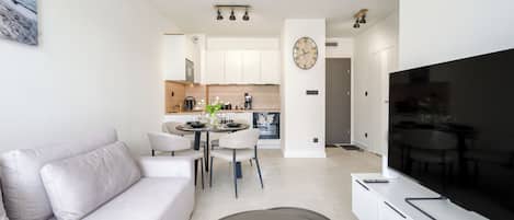 Una sala moderna con un sofá, un comedor con sillas y una mesa, una cocina con armarios y electrodomésticos, y un televisor de pantalla plana grande.