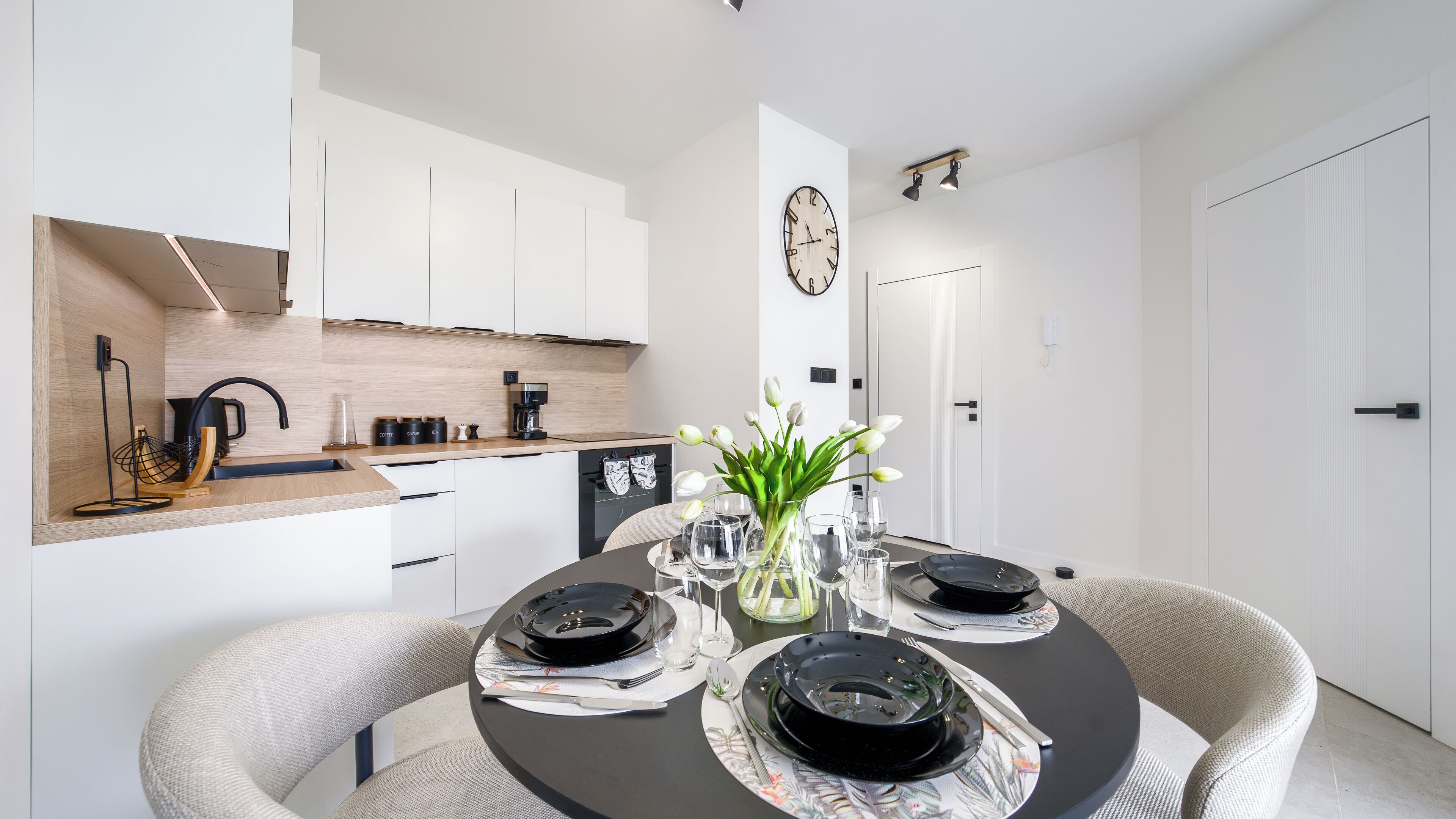 A modern kitchen with white cabinets, a coffee machine, and a dining area with a round table set for four.