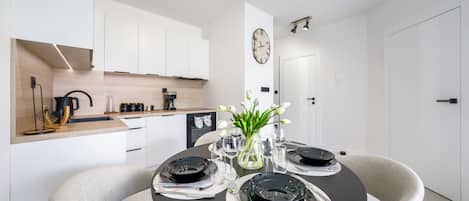 A modern kitchen with white cabinets, a coffee machine, and a dining area with a round table set for four.