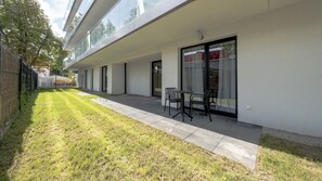 Een modern gebouw met een plat dak, grote ramen en een patio met een tafel en stoelen.