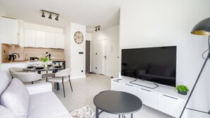 Ein modernes Wohnzimmer mit Flachbildfernseher, einer Couch, einem Essbereich mit Stühlen und einer Küche im Hintergrund.