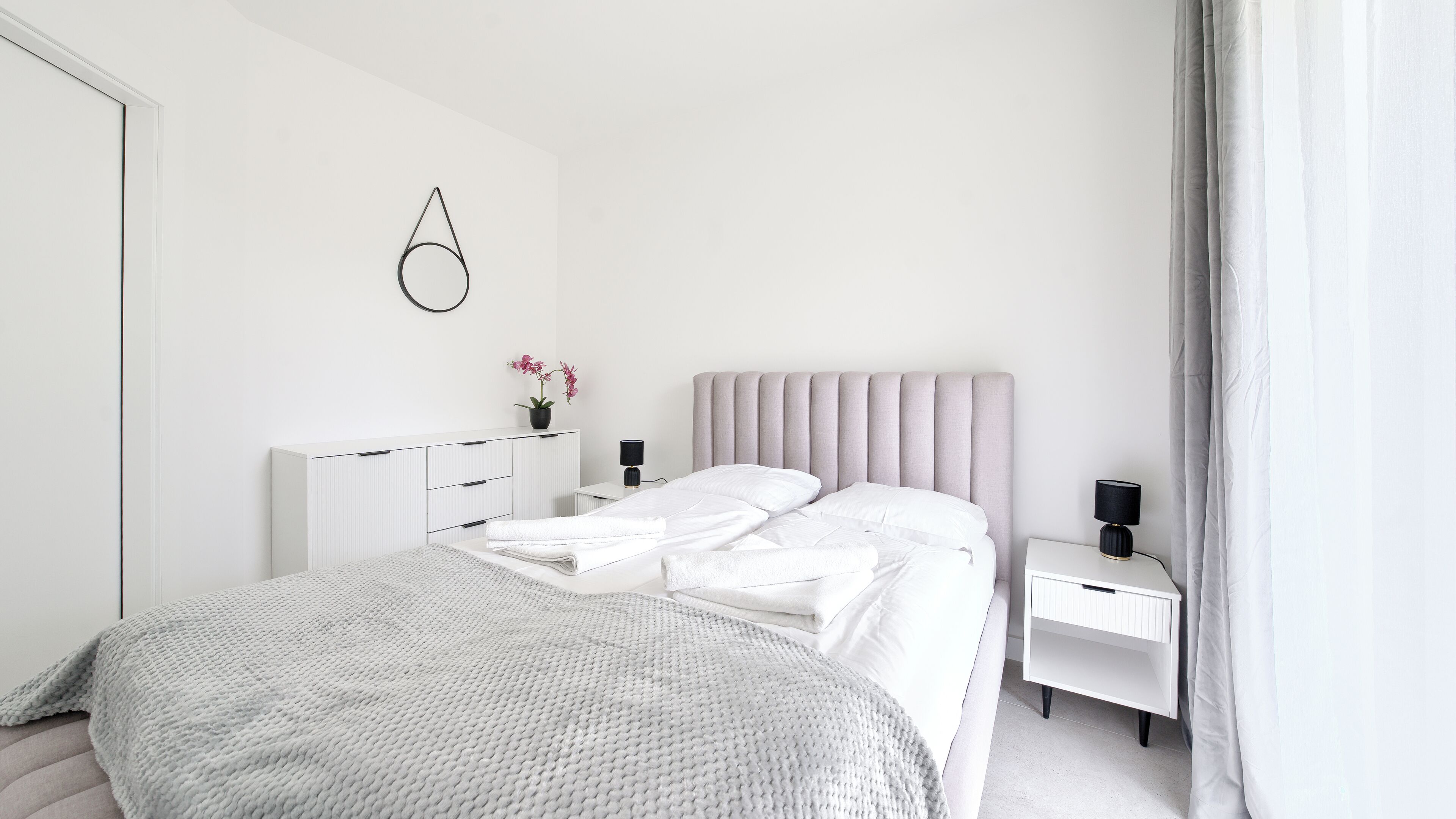 A modern bedroom with a bed, bedside tables, a radiator, and a wall-mounted light fixture.