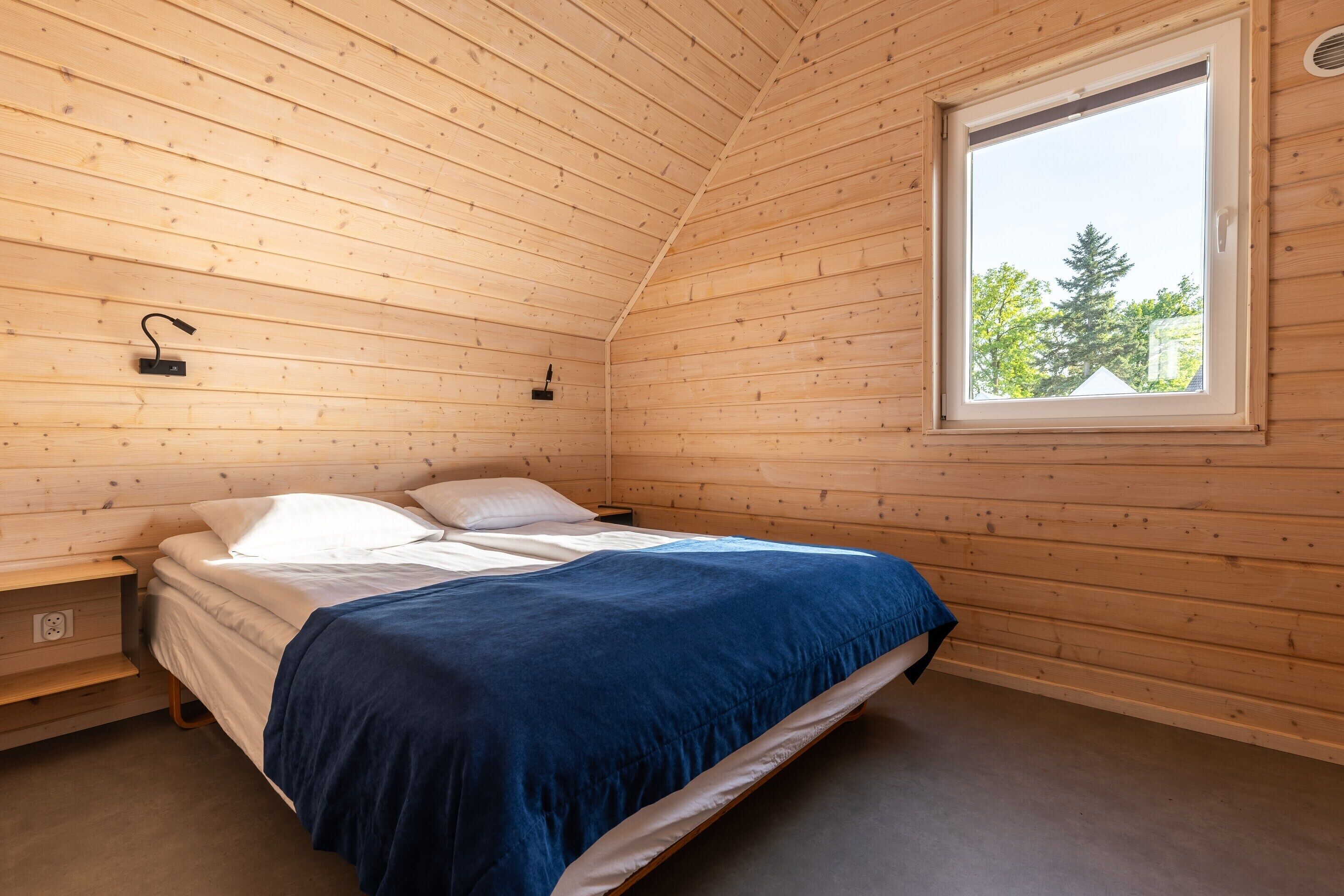 Una habitación de cabaña de madera con una cama, una ventana y una lámpara fijada a la pared.