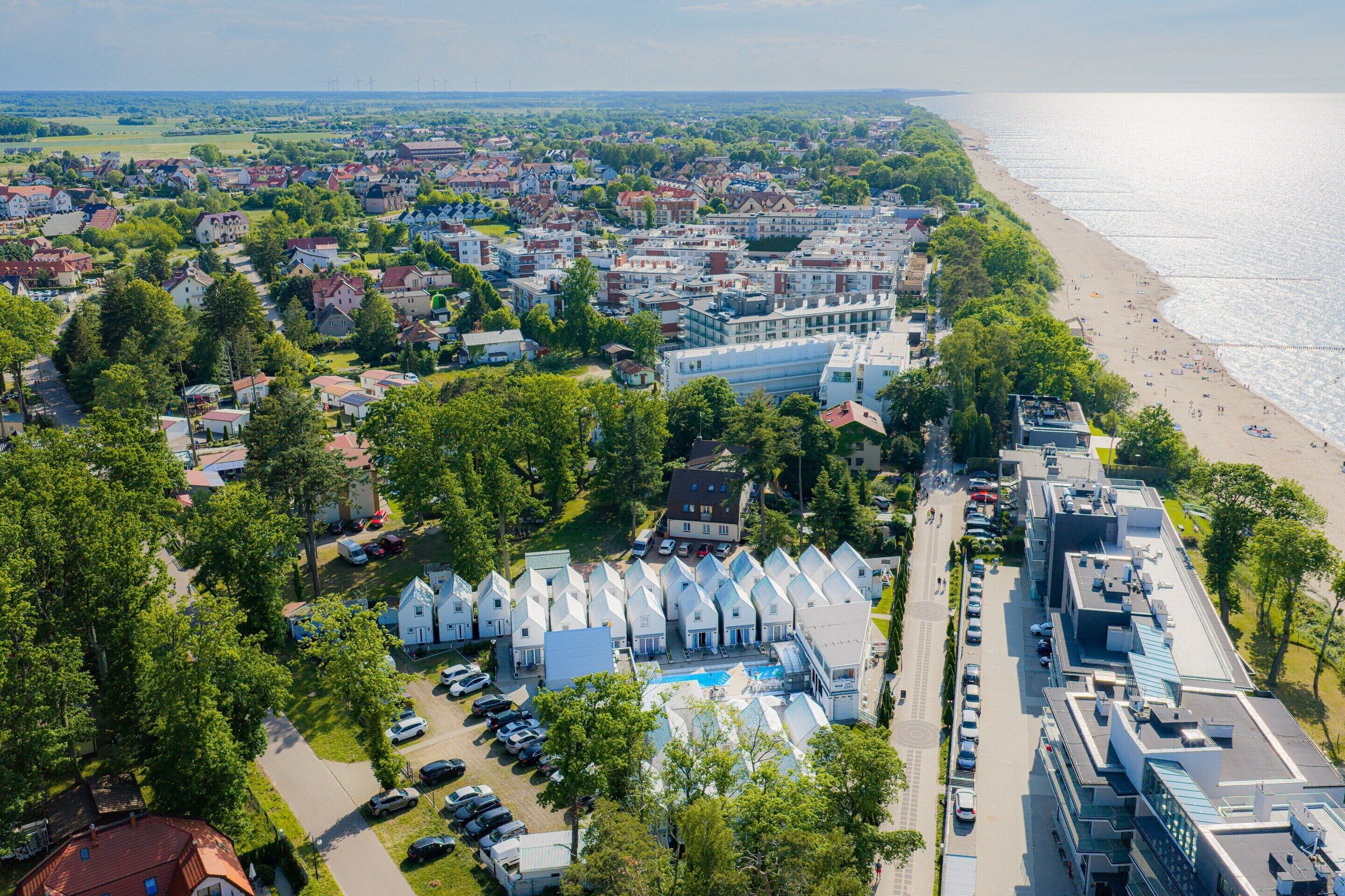 An aerial view of a coastal town with a beach, residential buildings, and a swimming pool area.