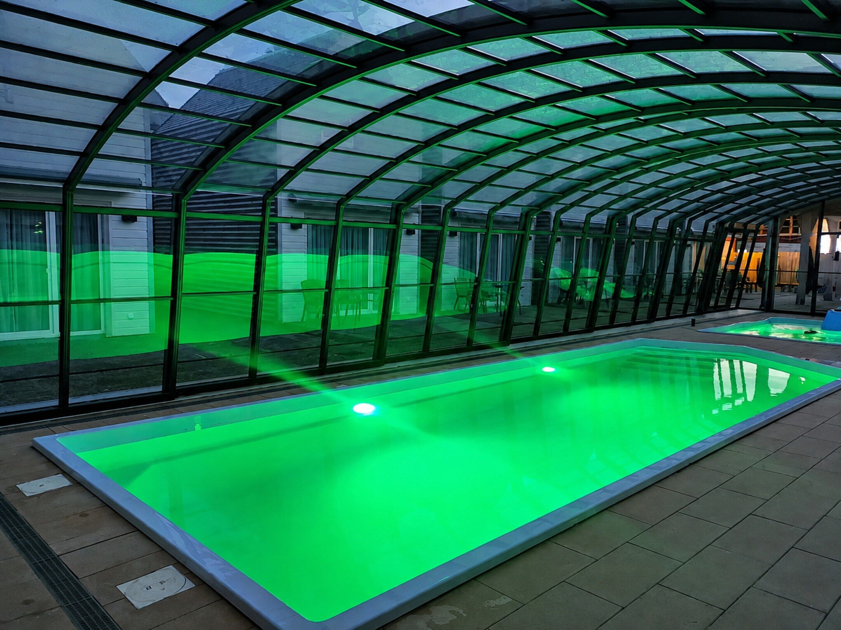 Une piscine dotée d’une structure en verre et d’un éclairage vert.