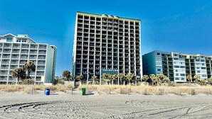 A beachfront hotel with multiple floors, a sandy foreground, and palm trees. - Oceanfront 1BR Sleeps 4-6 Myrtle Beach 421 (Myrtle Beach)