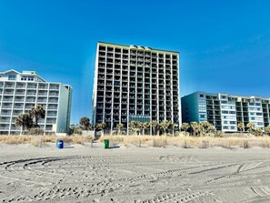 A beachfront hotel with multiple floors, a sandy foreground, and palm trees. - Oceanfront 1BR Sleeps 4-6 Myrtle Beach 421 (Myrtle Beach)