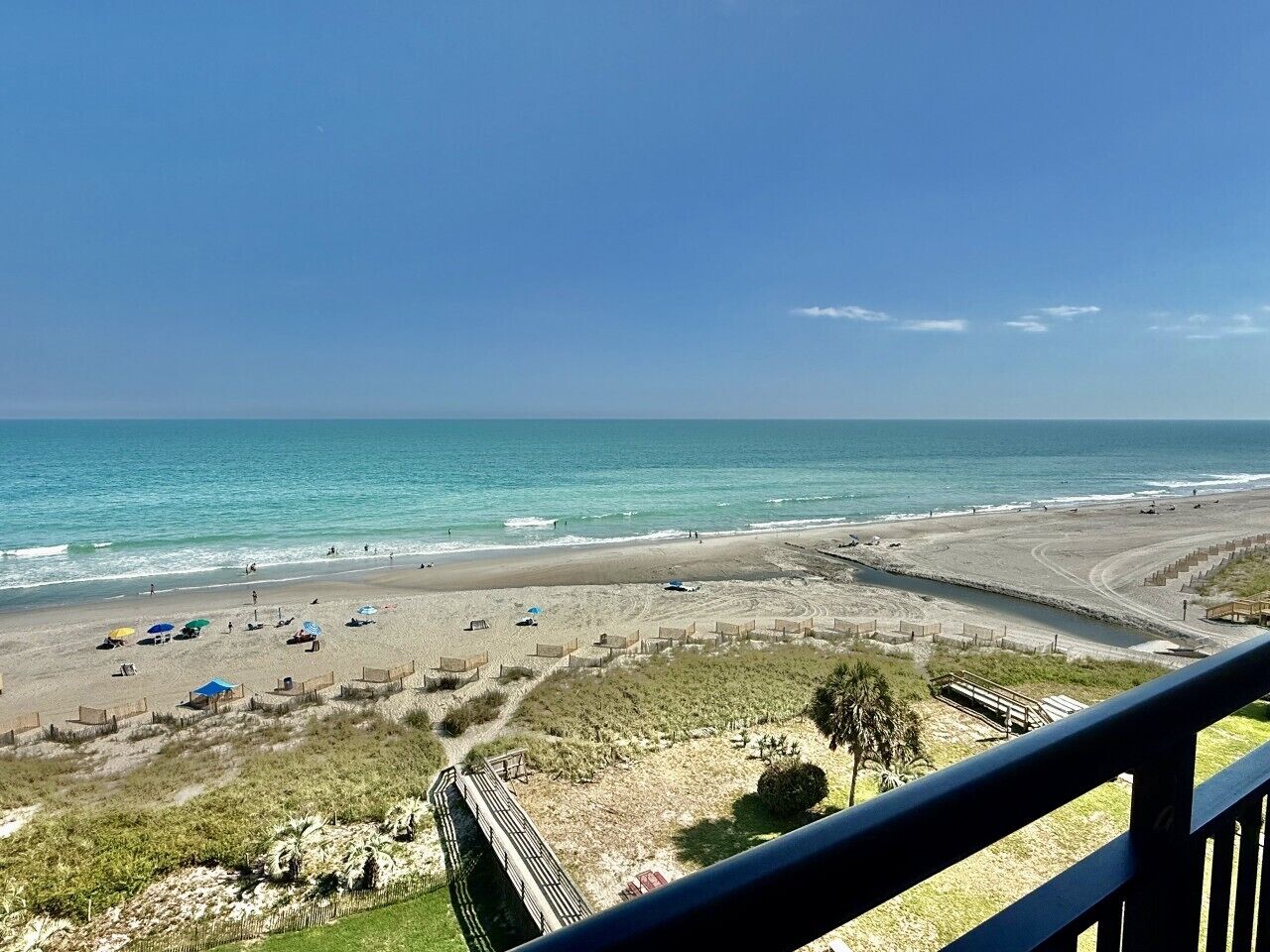 Ein Strand mit freiem Blick auf den Ozean, feinem Sand und einer Holzpromenade, die zum Wasser führt.