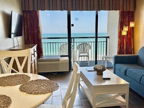 A room with a balcony, a TV, a table with woven placemats, a sofa, and a view of the sea. - Oceanfront 1BR Sleeps 4-6 Myrtle Beach 421 (Myrtle Beach)