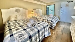 A hotel room with two beds, each with a checkered bedspread, a nightstand with a lamp, and a door with a handle. - Oceanfront 1BR Sleeps 4-6 Myrtle Beach 421 (Myrtle Beach)