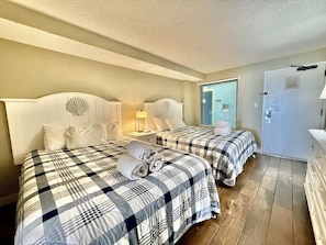 A hotel room with two beds, each with a checkered bedspread, a nightstand with a lamp, and a door with a handle. - Oceanfront 1BR Sleeps 4-6 Myrtle Beach 421 (Myrtle Beach)