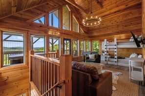A wooden cabin interior with a loft bed, seating area, and a view of the outdoors. - MTN Views|2 King Suites|Private|HotTub|Game Room|+ (Gatlinburg)