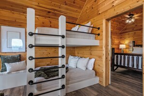 Uma cama beliche com escada, um sofá com almofadas e teto de madeira.