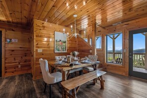 Un intérieur en bois avec une table à manger dressée pour quatre personnes, un lustre et un tableau accroché au mur.