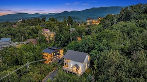 A residential area with multiple houses surrounded by dense forest and mountains in the background. - MTN Views|2 King Suites|Private|HotTub|Game Room|+ (Gatlinburg)
