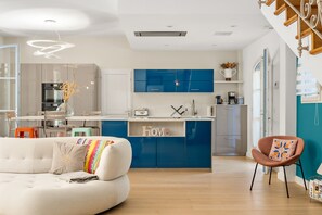 A modern kitchen with blue cabinets, a white sofa, and a dining area with a table and chairs. - Villa Jasmin | French Riviera Retreat (Vence)