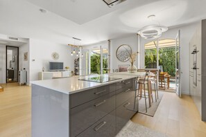 A modern kitchen with a large island, bar stools, and a view of the outdoors. - Villa Jasmin | French Riviera Retreat (Vence)