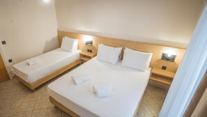 Une chambre d’hôtel avec deux lits simples et un lit plus grand, le tout agrémenté de draps et d’oreillers blancs.