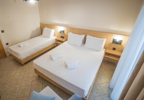 Ein Hotelzimmer mit zwei Einzelbetten und einem größeren Bett, alle mit weißen Laken und Kissen.