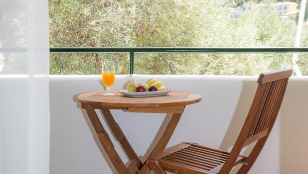 Un ensemble de table et de chaise en bois est installé sur un balcon d’où l’on peut admirer les arbres et les bâtiments.