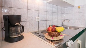Une petite cuisine équipée d’une machine à café, d’un panier de fruits et d’un évier.