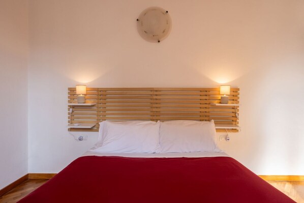 Ein Bett mit Holz-Kopfteil, zwei Wandlampen und einer roten Bettdecke.