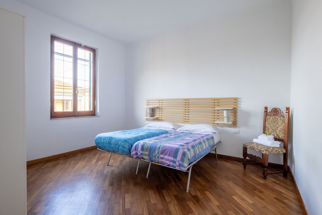 Ein Zimmer mit zwei Betten, Holzboden, einem Fenster und einem Sessel mit Handtüchern.