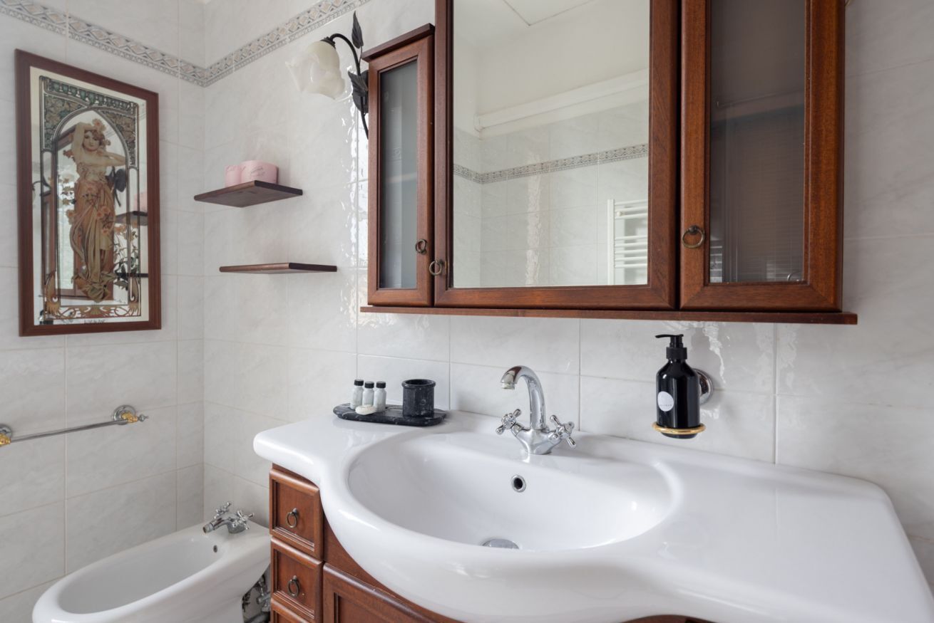 Ein Badezimmer mit einem weißen Waschbecken, einem Spiegel und einem Holzkabinent.