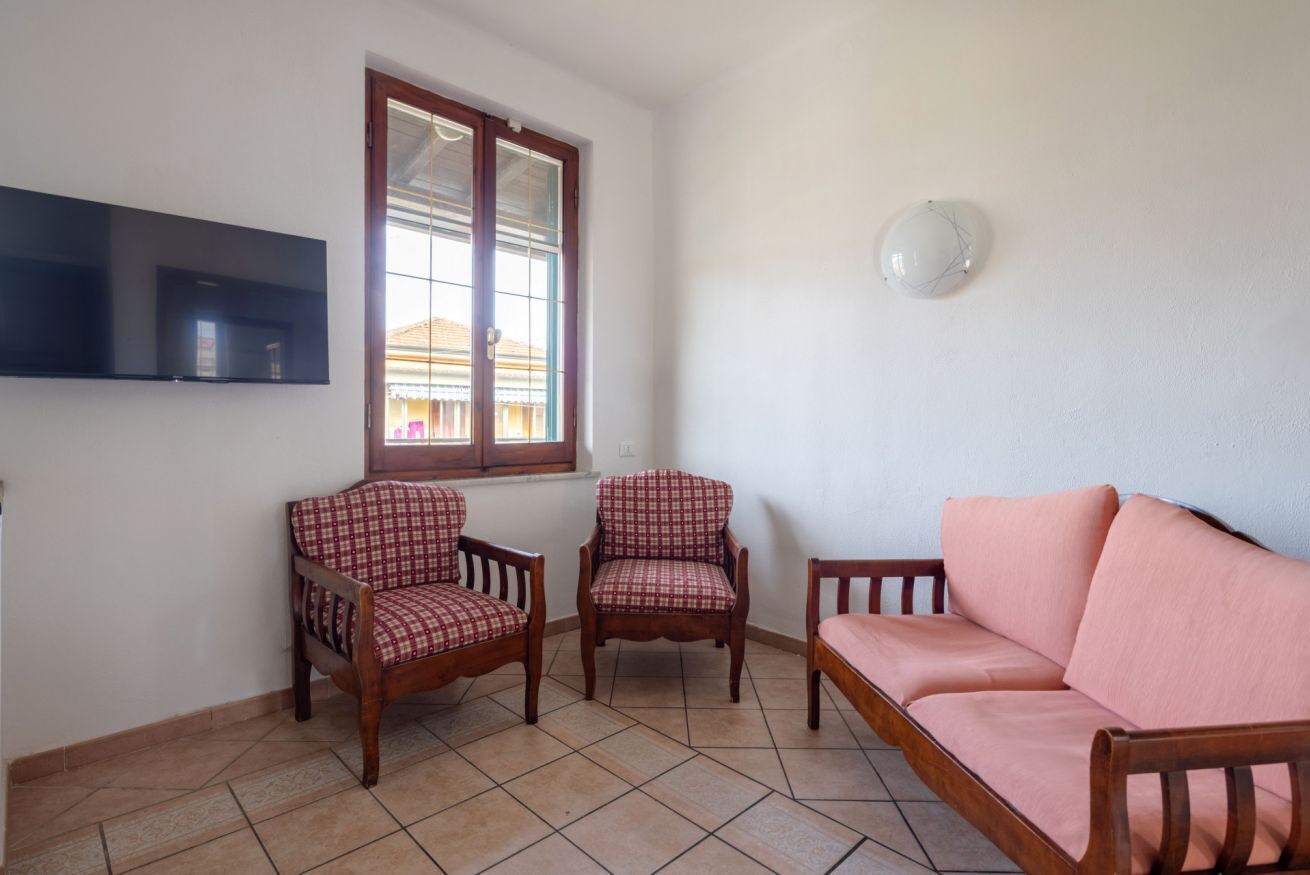 A living room with a sofa, two armchairs, a TV mounted on the wall, and a window with blinds.