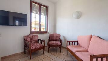 A living room with a sofa, two armchairs, a TV mounted on the wall, and a window with blinds.