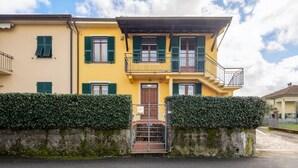 Un edifici de dues plantes amb façana groga, persianes verdes i entrada tancada per una reixa.