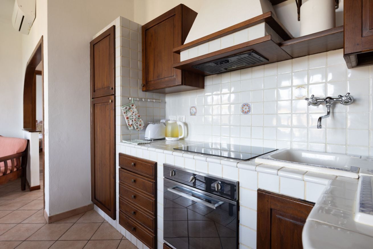 Cocina con armarios de madera, horno de acero inoxidable y salpicadero de azulejos blancos.