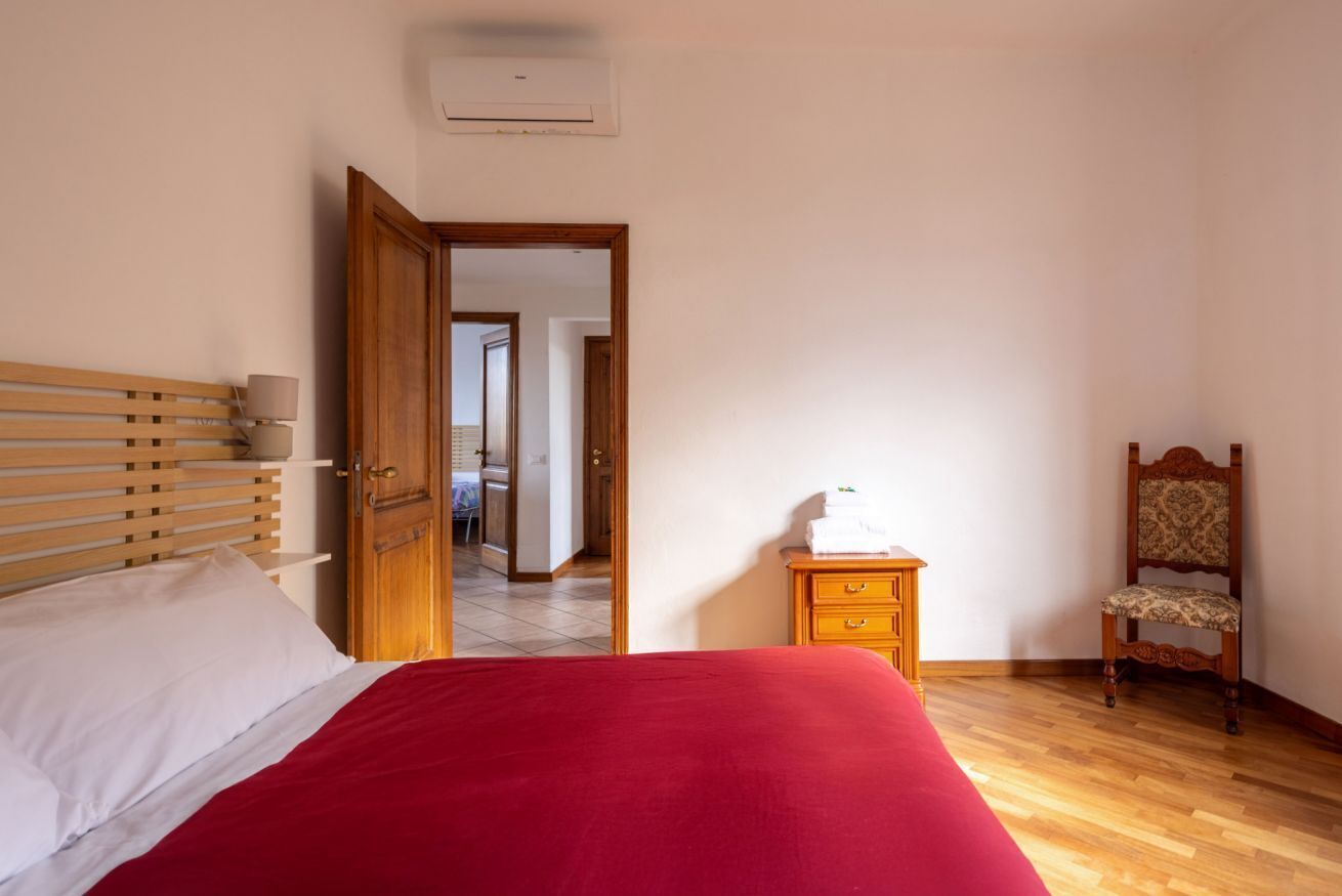 A bedroom with a bed, a wooden nightstand, a chair, and a door leading to another room.